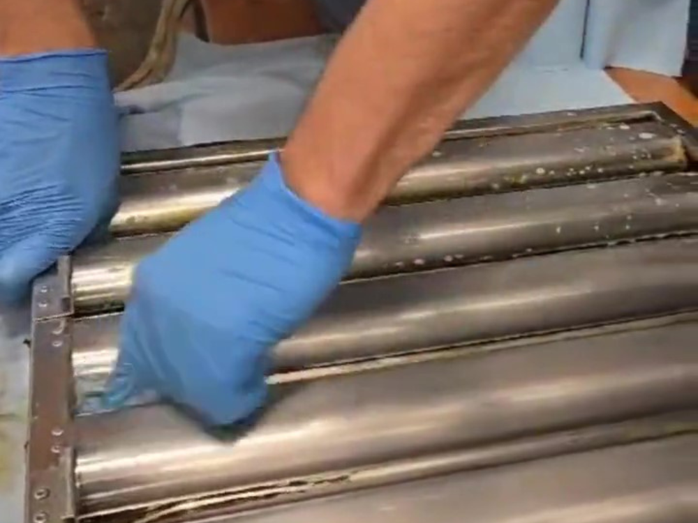 Technician performing commercial exhaust cleaning on metal filters using blue gloves.