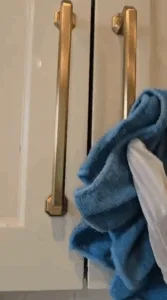 Complete Kitchen Cleaning: Close-up of a hand cleaning the cabinet handles with a blue towel.